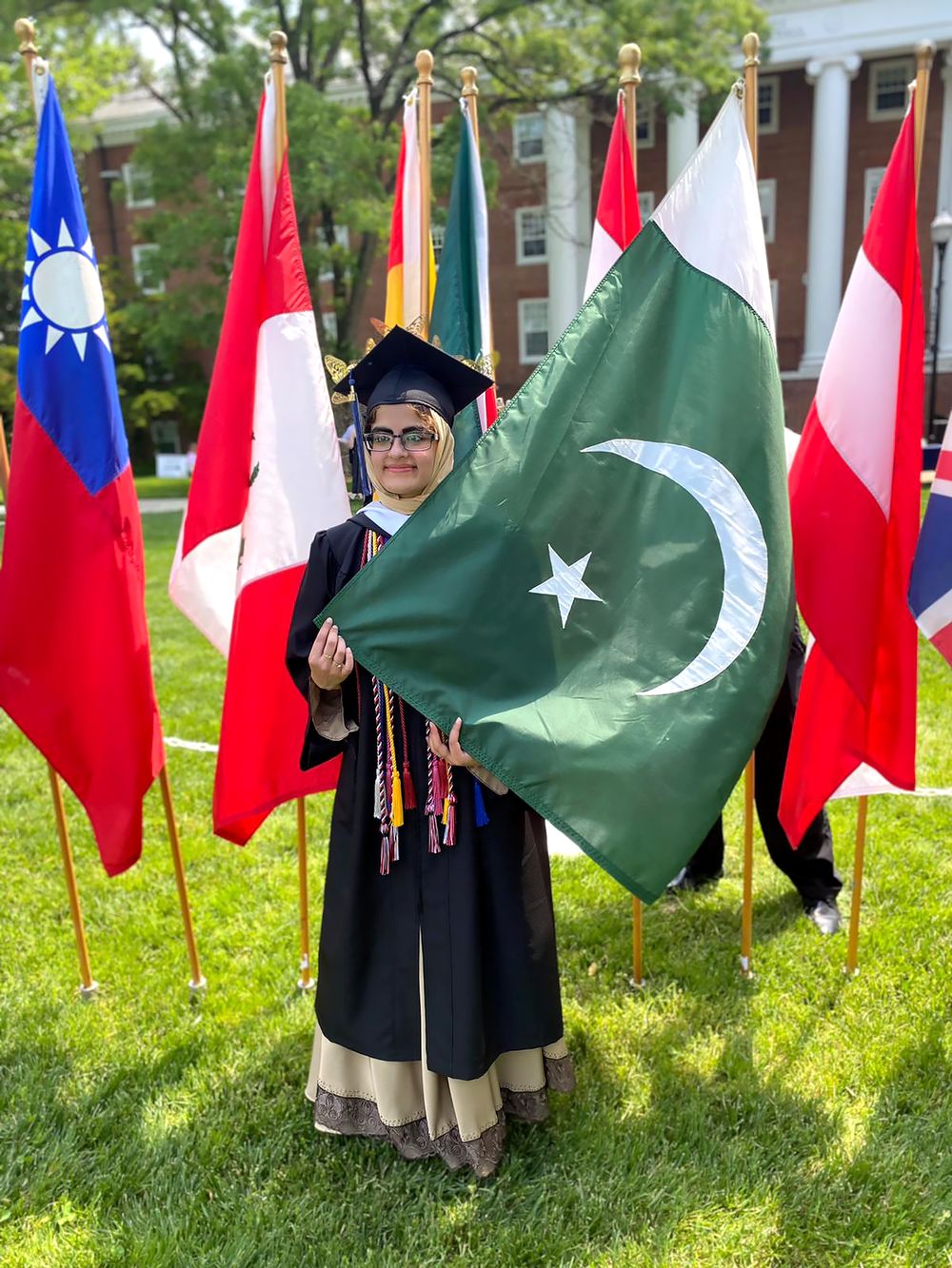Maryam at graduation holding the Pakistani flag among world flags